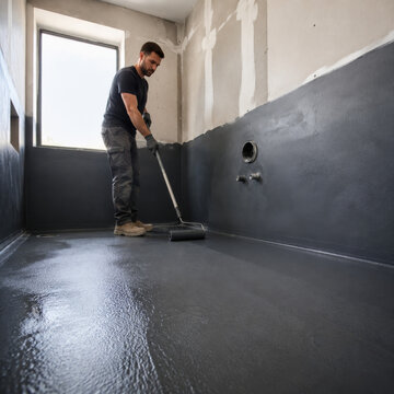 Trabajador aplica pintura en el suelo de una habitaci&oacute;n en construcci&oacute;n mientras se prepara para finalizar el proyecto
