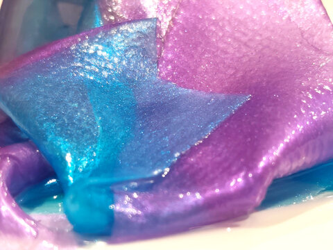 Soft-focus close-up of iridescent purple and blue translucent material, creating abstract flowing shapes with a smooth, shimmering texture.
