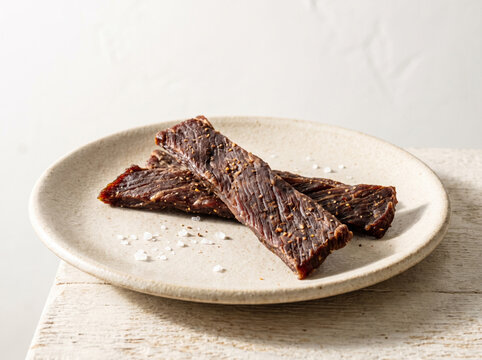 Strips of seasoned beef jerky served on a ceramic plate with sea salt