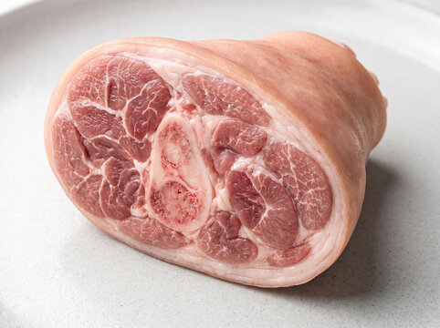 Raw pork knuckle cut in half showing bone and marbled meat on a plate