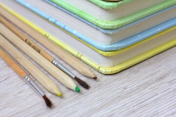 Fototapeta premium Stack of colorful books with pencils and paintbrushes on a wooden table, school learning, creativity, studying