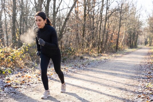 Woman running outdoors in forest on a frosty morning, showing breath vapor