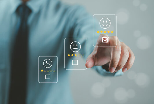 The hand is giving a five-star rating. The business person selects the smiley face icon on the virtual screen to express their satisfaction with the service. The rating received is very impressive.