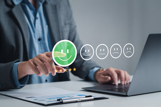The hand is giving a five-star rating. The business person selects the smiley face icon on the virtual screen to express their satisfaction with the service. The rating received is very impressive.