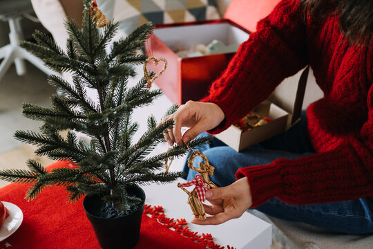 Woman hands hang straw ornament on branch of small potted tree on table. Handmade rustic christmas ornaments, organic tree decoration style, zero waste christmas decor concept