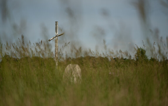 Old weathered wooden Christian cross and a headstone looking through out of focus grass
