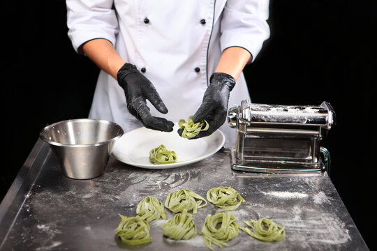 Cook cooks with black gloves, forming nests of fresh homemade pasta with spinach. Paste has green color. Natural dyes. Table top is meta.