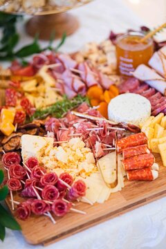 Charcuterie board arranged, in indoor, with cheese, meats, fruits, herbs, with brown, white accents.