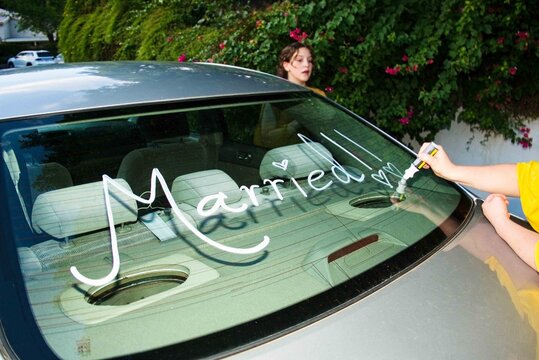 child writing playful message on car windshield in residential area side view family activity fun.a.