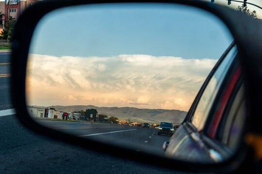 car side mirror reflects roadside town with mountains in background, peaceful scene inside car view.