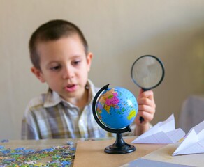 Young boy examining a world globe with a magnifying glass - Curious student learning geography and exploring the map with a magnifier © light