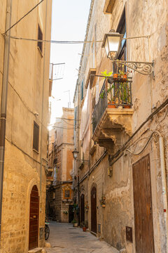 Narrow alley in Bari old town, Italy, with weathered stone buildings, ornate balcony with potted plants and vintage lantern, concept of southern Italian architecture