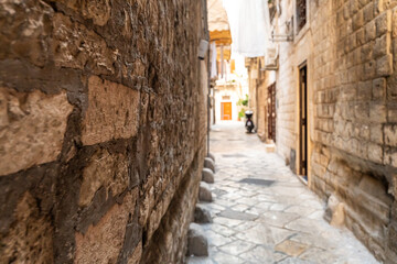 Obraz premium Narrow alley in Bari Italy old town with weathered stone walls and cobblestone pavement, leading to distant orange door in historic Mediterranean district