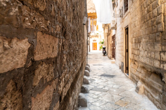 Narrow alley in Bari Italy old town with weathered stone walls and cobblestone pavement, leading to distant orange door in historic Mediterranean district
