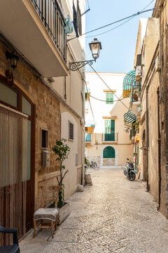 Narrow alley in Bari old town, Italy, with cobblestone pavement, cream-colored facades, green shutters, and a parked scooter in warm afternoon light