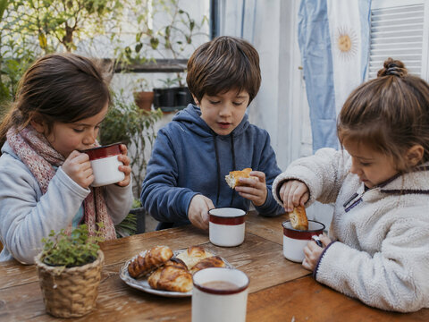 Children Having an Afternoon Snack with Medialunas and Warm Drinks