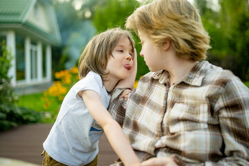 Fototapeta premium Playful young boy teasing his older sister outdoors in the garden. Funny candid moment of sibling interaction and playful family relationship.