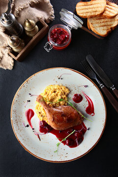 Baked duck leg with cherry sauce. Cherry sauce in small jar. An exquisite dish. Slices of white bread. Top view.