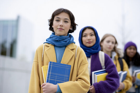 Diverse group of teenage student girls holding books standing outdoors near school building