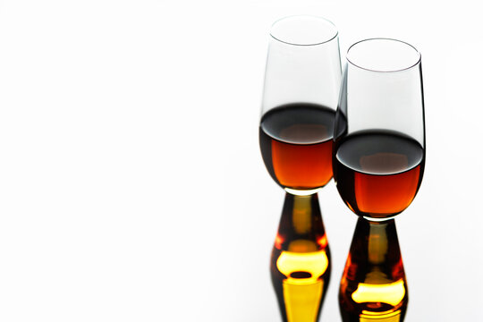 Two glasses of amber alcoholic beverage against white background with perfect reflection. Close-up studio photograph of alcoholic beverages. Four glasses are arranged in neat row on mirrored surface. 