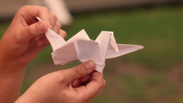 Child hands holding a moving origami crane made from folded paper