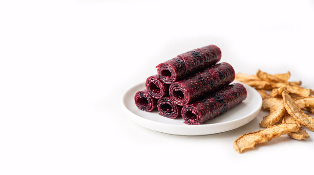 Healthy snack flat lay with homemade raspberry fruit leather rolls and dried apple slices on light background