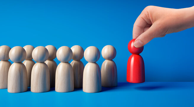 Wooden figurines in a group with hand placing one red figure stands out as leader or speaker on blue background - 3D illustration - not ai generated	
