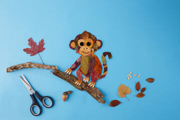 Monkey made from autumn leaves sitting on a branch. Autumn nature and children creativity concept. Design for poster, print, greeting card, postcard. Flat lay composition with copy space © Elena