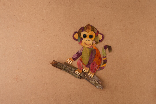 Monkey made from autumn leaves sitting on a branch. Flat lay craft photography. Autumn nature and children creativity concept. Design for poster, print, postcard. Flat lay with copy space
