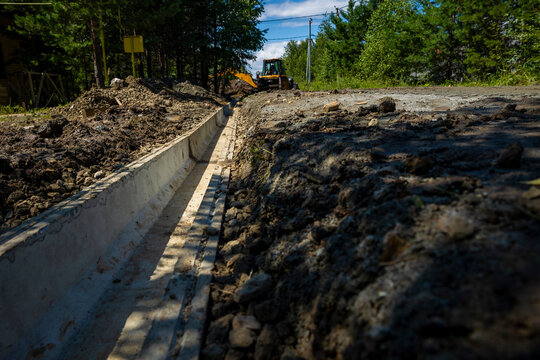 Installed concrete drainage gutter channel on ground side of rural road. Concept: stormwater drainage system