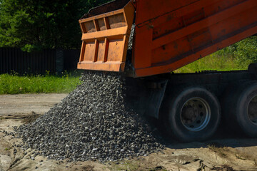 Orange dumper truck unloading crushed stone gravel on geotextile at construction site. Concept: aggregates supply industry © Marya