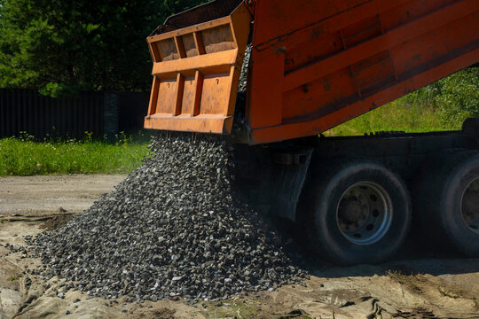Orange dumper truck unloading crushed stone gravel on geotextile at construction site. Concept: aggregates supply industry