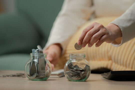Saving money concept. Anonymous person calculating budget and putting coin into savings jar for emergency fund at home with calculator and notebook. Savings, budget, finance, emergency, planning