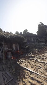 Houses made of wood are seen in an open area. Some barrels are placed around. The ground is dry. The sun shines brightly. Trees are visible in the background.