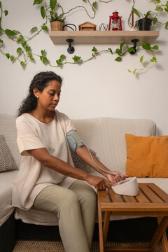 vertical young Hispanic woman measuring blood pressure at home