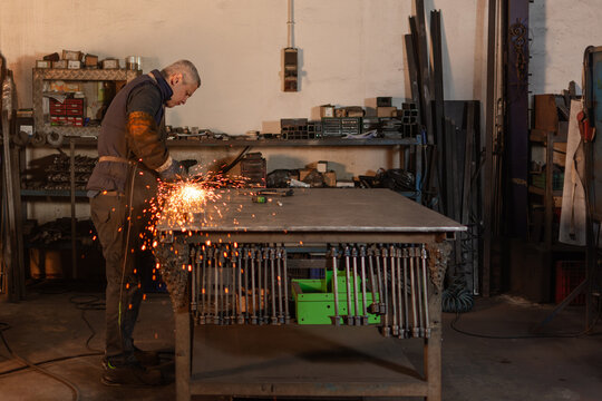 Full body industrial worker grinding metal with electric grinder and sparks