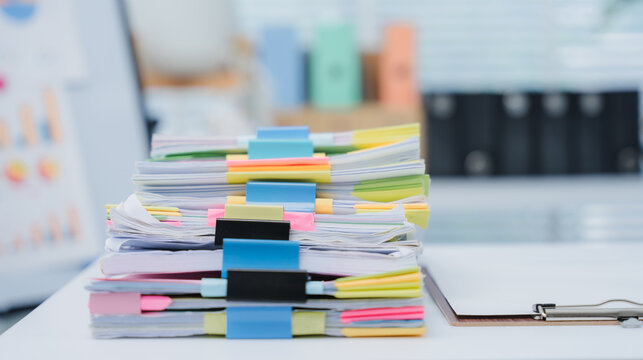 Workplace Documentation: A close-up shot of an office worker in a tailored blue blazer, meticulously reviewing a stack of documents.	