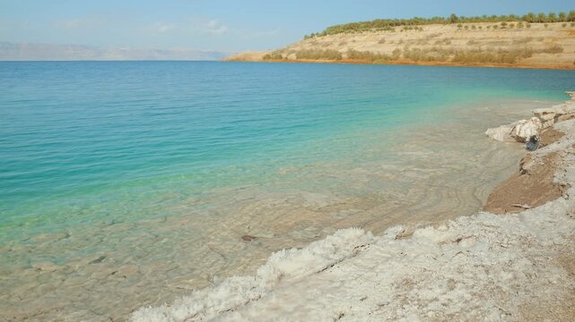 Calm clear turquoise water at shore of Dead Sea on Jordan side, mountains far background are Israel