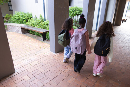 African American female students walking along brick corridor, carrying colorful backpacks