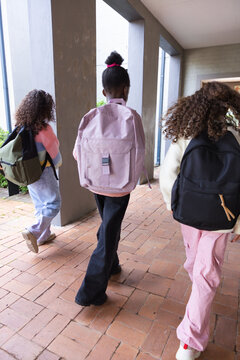 African American teenage girls walking through school corridor carrying pink olive black backpacks