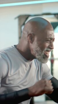 Vertical video: Smiling man in gray shirt punching and rotating torso for training in gym, rack