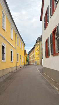 A long narrow straight empty street in Speyer, with small colourful cottages with shuttered blinds.