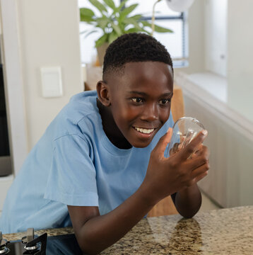 African teen male leaning over granite kitchen counter, holding clear glass orb, smiling