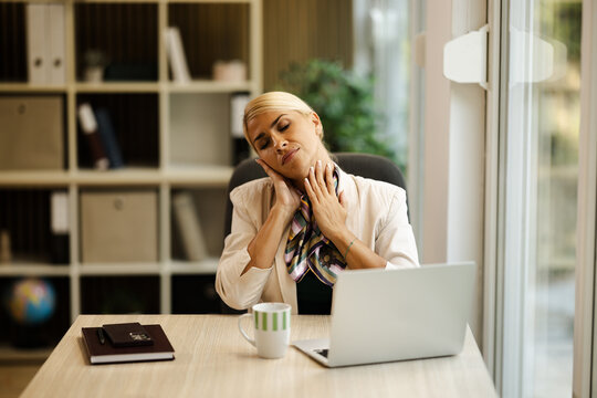 Woman Working in a Small Office While Showing Signs of Discomfort in Her Neck