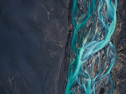 Aerial top-down view of turquoise glacial river streams flowing through dark volcanic sand in Iceland, creating abstract natural patterns