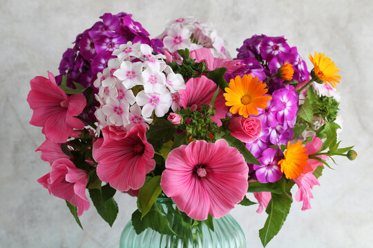 Colorful bouquet of pink lavatera, purple phlox and orange calendula flowers in glass vase