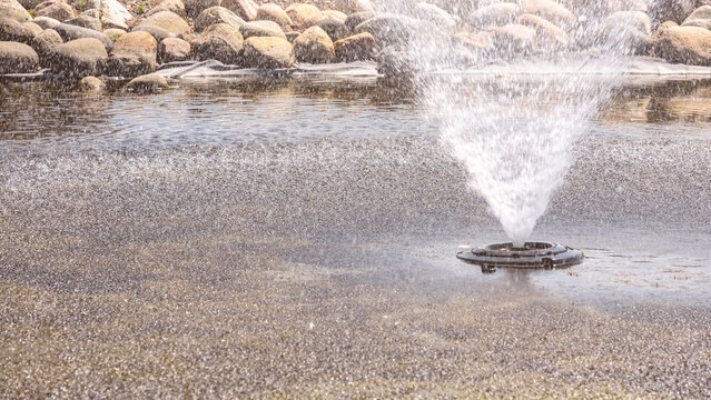 Pond Water Fountain Spraying with Rocky Edge Background. Water Management and Aeration landscape banner