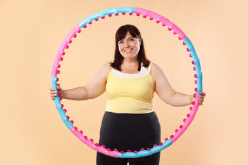 Overweight woman with hula hoop on beige background. Sports equipment © New Africa