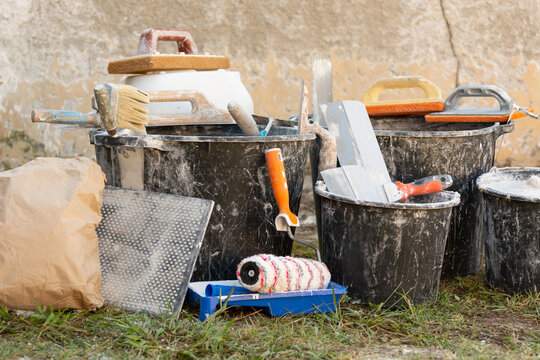 Construction buckets with plaster residue, trowels, paint roller and dry mix outdoors during home renovation and interior finishing work. Concept: home renovation, materials, prices and repair costs.
