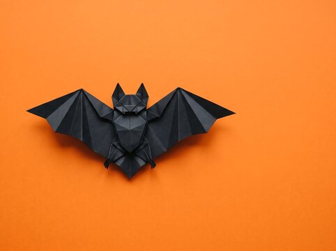 A single black paper origami bat isolated on a vibrant orange background